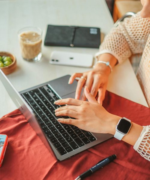 Close-up of a woman working on a laptop with a smartwatch, emphasizing modern technology and productivity at a cozy desk.