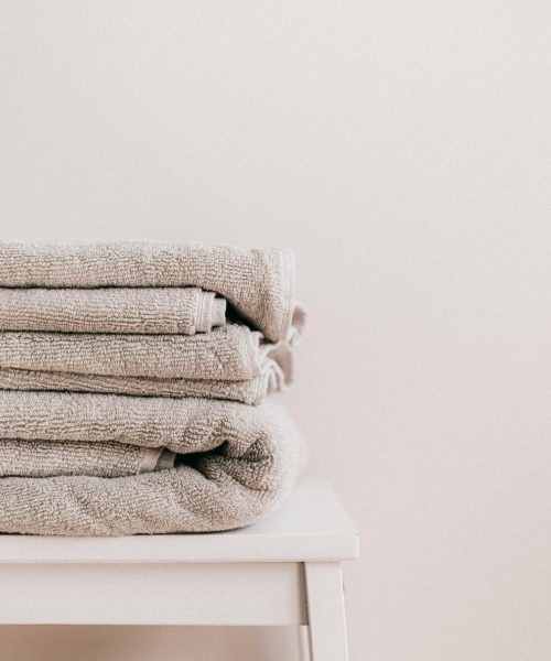 Stack of soft clean fresh gray towels placed on white minimalist stool against beige wall